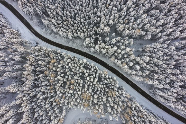 drone aerial birdseye shot of winter country road through forest with snow covered trees glaze ice