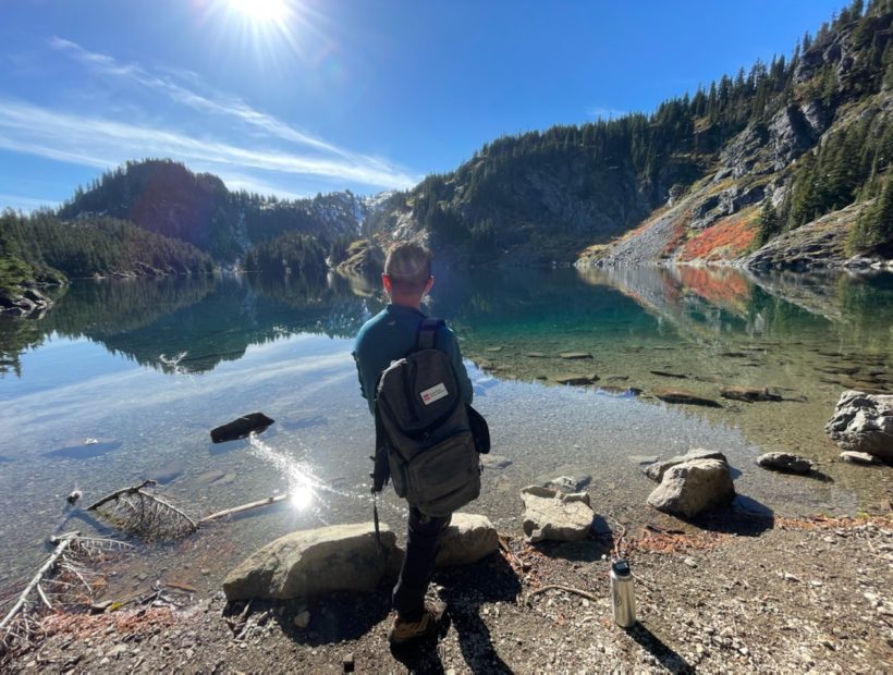 Male hiker with backpack looks out at lake and mountain landscape