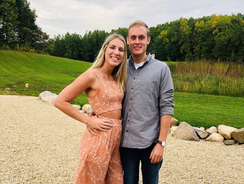 A blonde couple, both TNAA travel nurses, pose together outside on a gravel and grassy landscape.