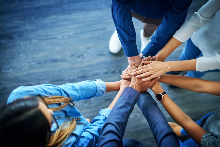 High angle shot of a group of colleagues joining their hands together in unity